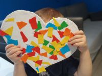 Piąte zdjęcie przedstawia serce wykonane przez Kacpra Termolika. Na białym sercu naklejono kolorowe wycinanki z papieru kolorowego. Chłopiec trzyma serce w dłoniach.